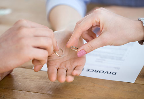 Hands exchanging wedding rings over a divorce document, representing legal support for separation.