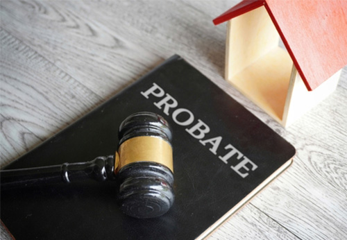Gavel resting on a black binder labeled PROBATE next to a small wooden house, symbolizing legal issues related to estate property