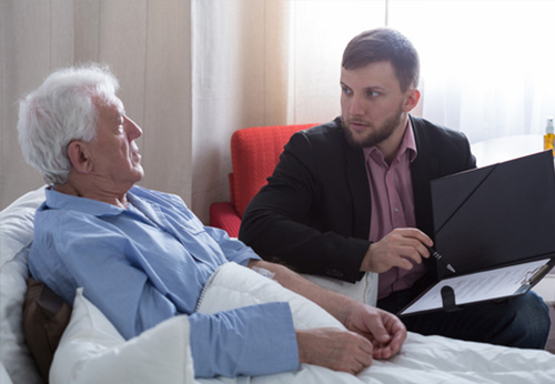 An elderly man in bed speaking with an attorney reviewing documents, discussing conflict during probate
